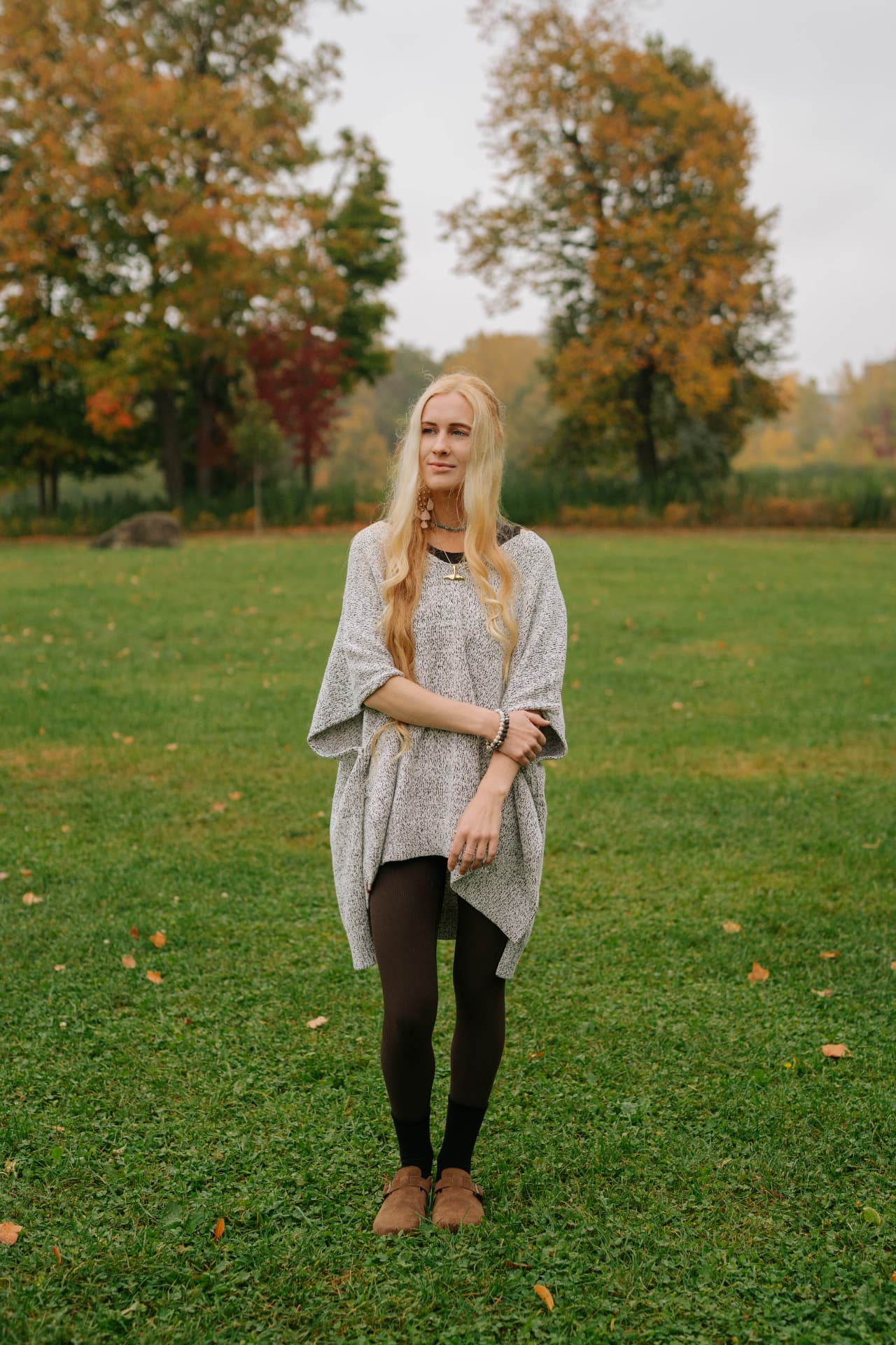 Sarah standing in a grassy field with autumn trees behind her